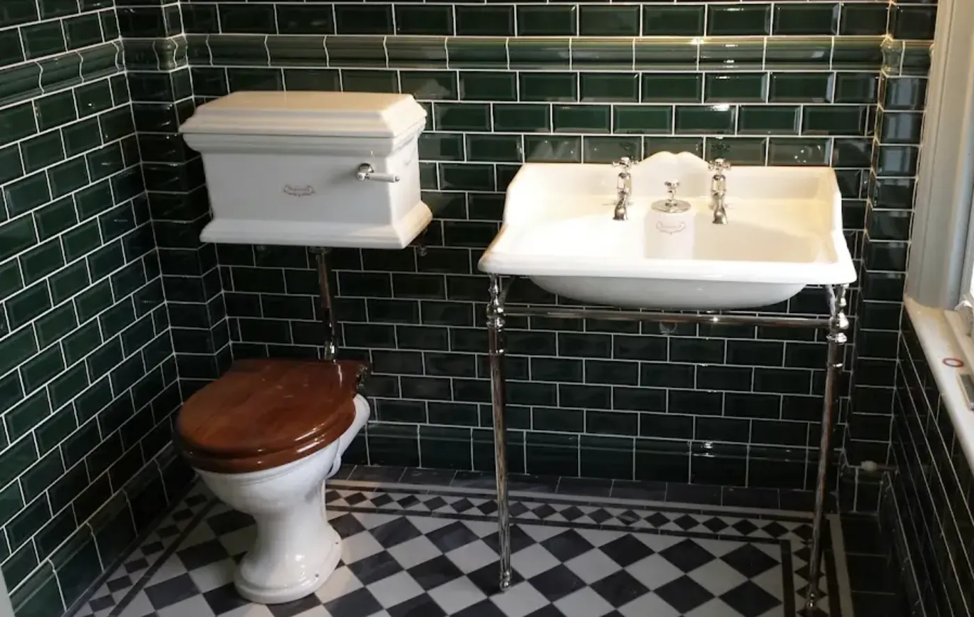 Cloakroom tiled in dark green bevelled metro with a traditional high level cistern and basin