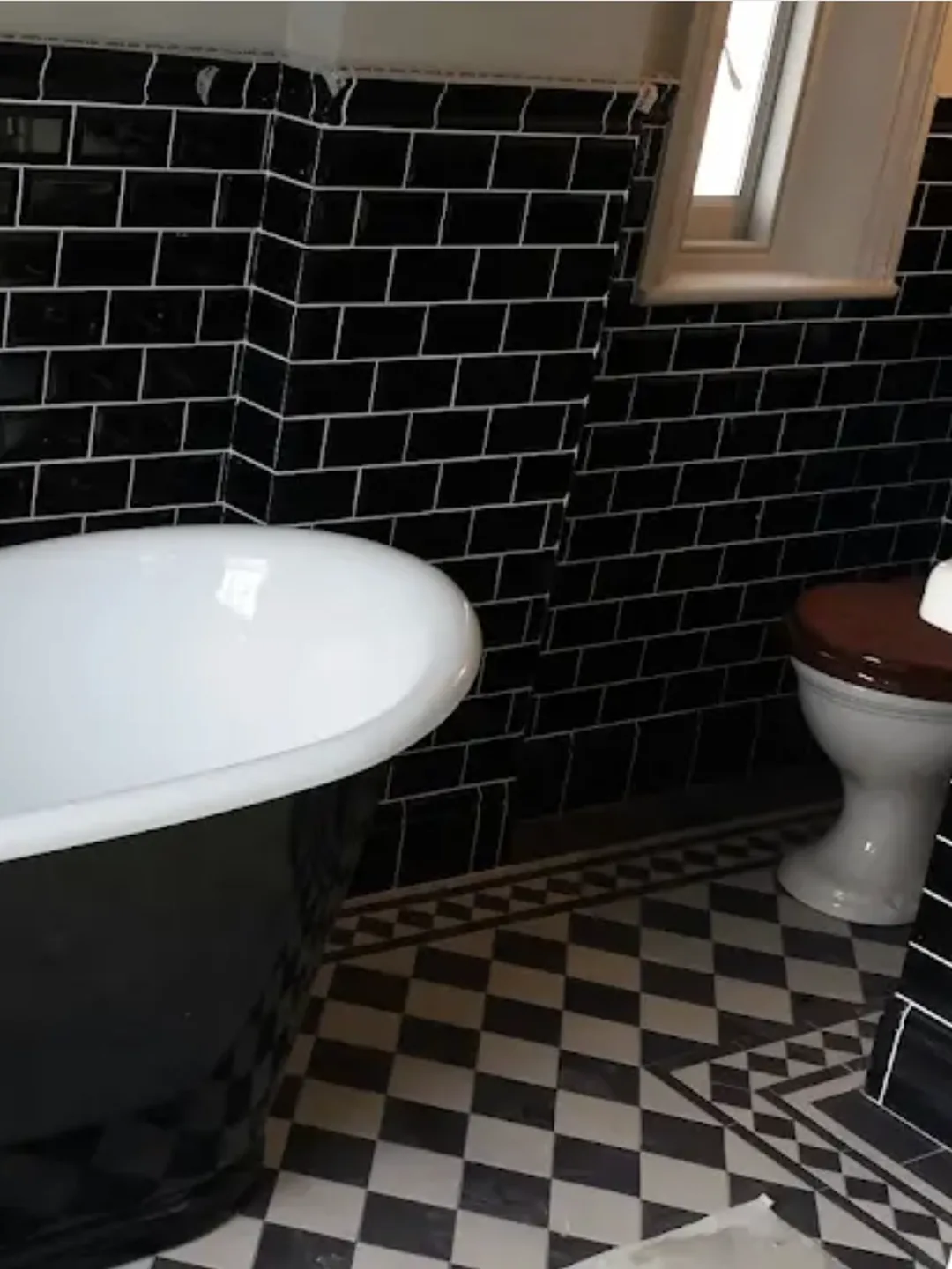 Black metro tiled bathroom with a roll-top bath and a black and white checkerboard floor