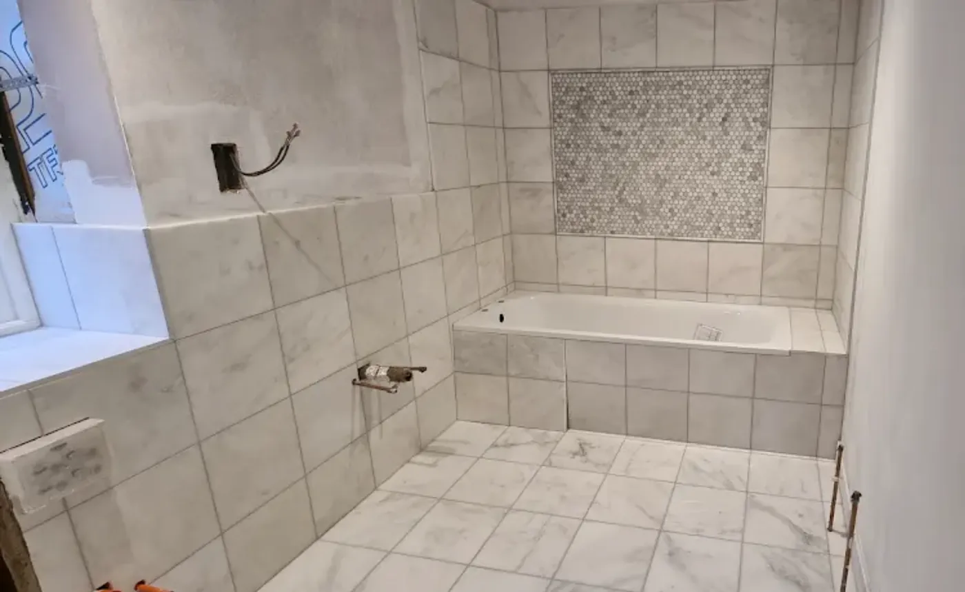 Bathroom tiled in large marble tiles with a bath surround and a hexagon mosaic inset panel