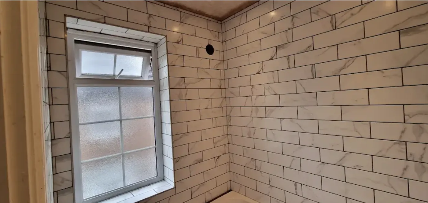 Shower room walls in marble effect metro tiles run to the ceiling around a window