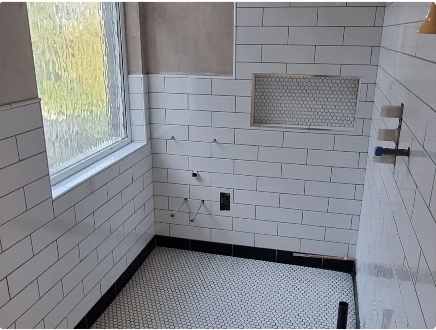 White metro tiled bathroom with a recessed hexagon mosaic niche and a black tile border